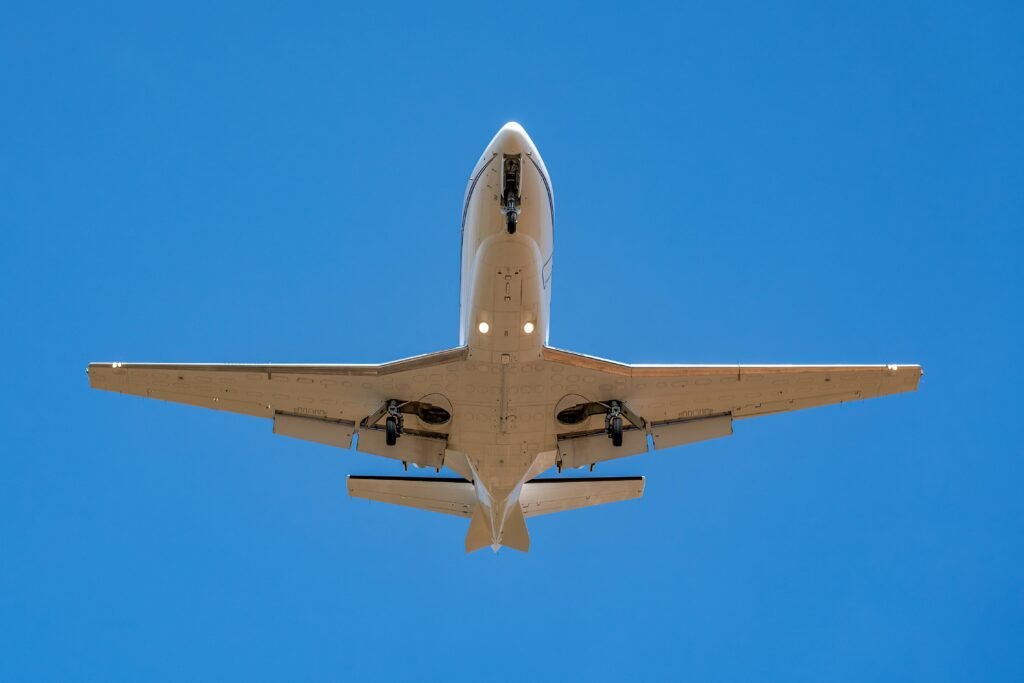 A private jet soaring overhead with landing gear visible against a clear blue sky.