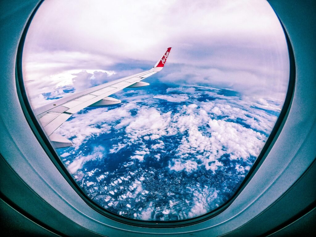 Wide angle of rocky ground through cloudy sky and plane wing from window of aircraft
