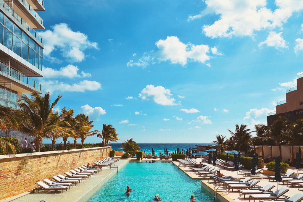 Serene beachfront pool area at a luxury resort in Cancun, Mexico, with palm trees and blue skies.