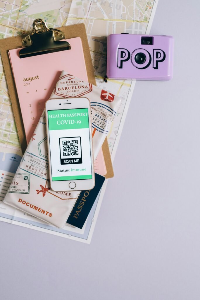 Flat lay of travel essentials with smartphone health passport, camera, map, and documents.