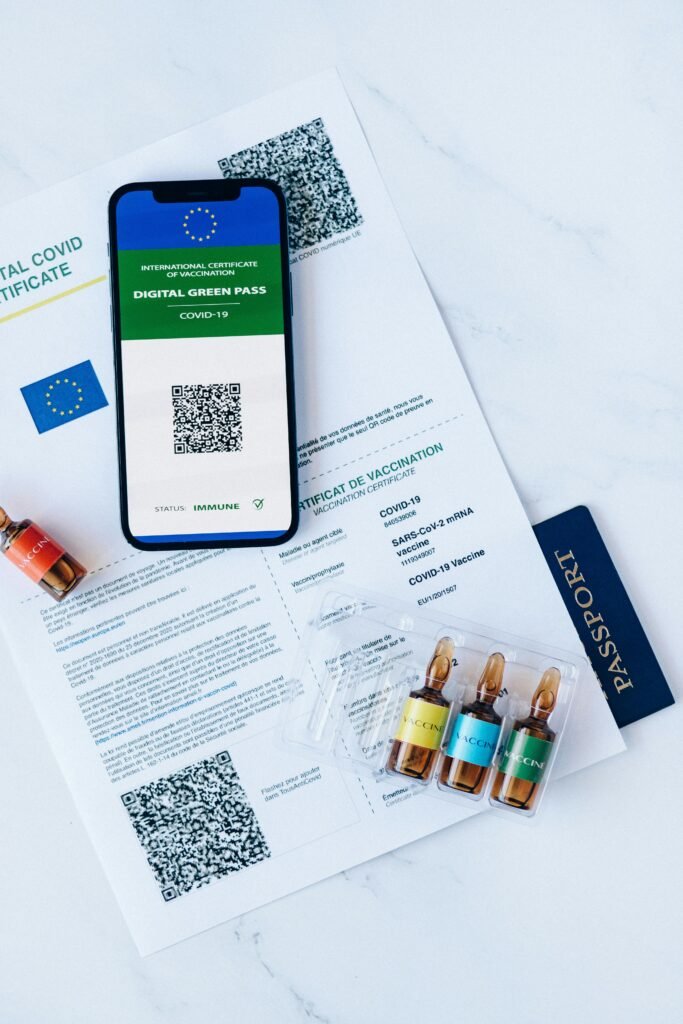 COVID-19 digital green pass with ampoules and EU passport, flat lay on marble.