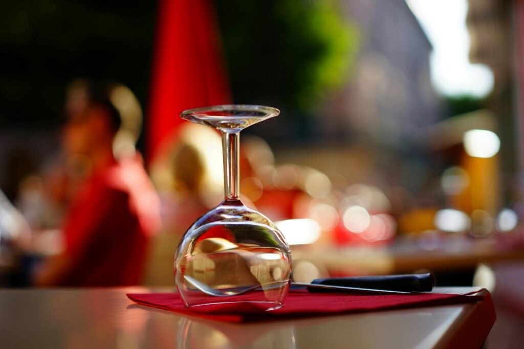 Upside-down wine glass on a vibrant red napkin in an outdoor cafe setting with blurred people in the background.
