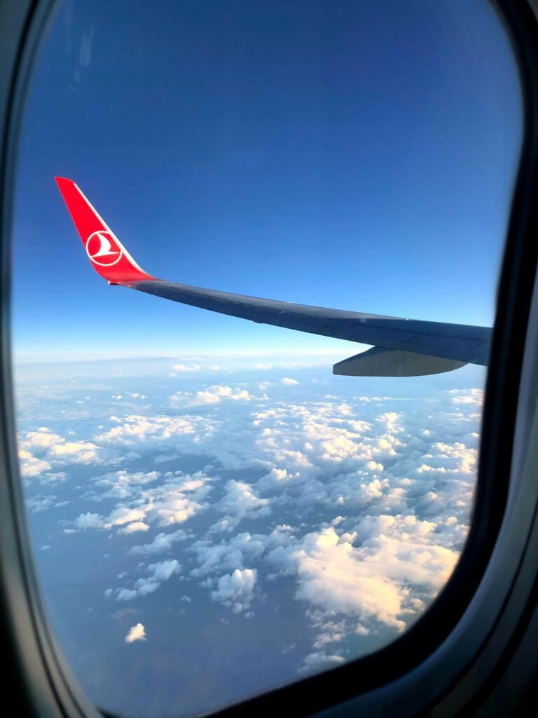 View from an airplane window showcasing the wing, clouds, and a clear sky.